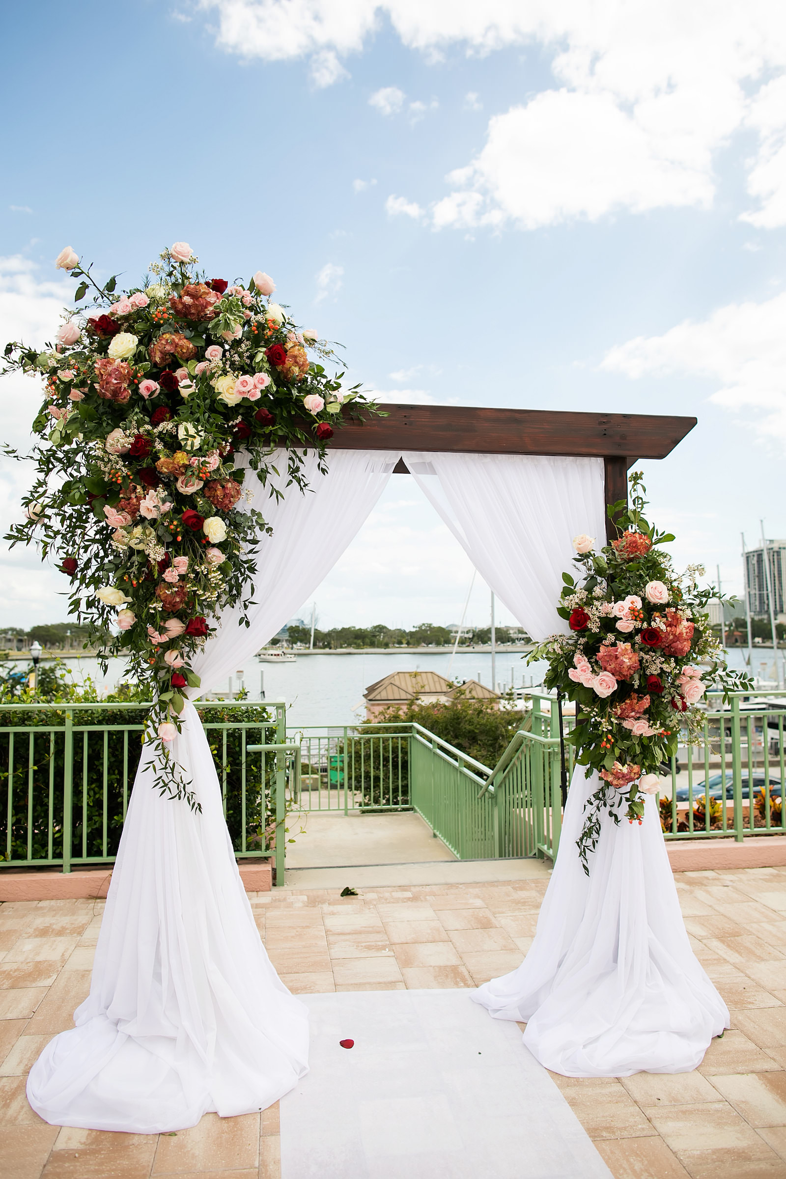Elegant Garden Wedding Ceremony Decor, Wooden Arch with Lush Burgundy and Pink Floral Arrangements and White Linen Draping | Tampa Bay Wedding Photographer Limelight Photography | Planner Breezin Weddings | Florist Lemon Drops | Rentals Outside the Box Event Rentals | Downtown St. Pete Venue The Vinoy