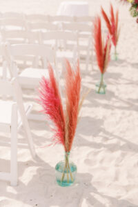 Vibrant Boho Beach Wedding, Red and Hot Pink Pampas Grass in Glass Vases Lining Wedding Ceremony Aisles