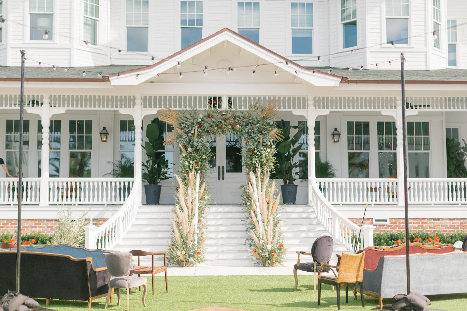 Boho Garden Wedding Ceremony Decor, Lounge Seating, Vintage Couches, Lush Greenery and Floral Arch with Pampas Grass Arrangements, String Lights | Tampa Bay Wedding Planner Parties A'la Carte | Florida Wedding Venue Belleview Inn