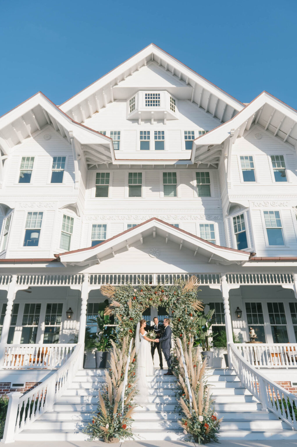 Boho Garden Wedding Ceremony, Bride and Groom Exchanging Wedding Vows Outside Florida Mansion Belleview Inn, Lounge Seating, Vintage Couches, Lush Greenery and Floral Arch with Pampas Grass Arrangements, String Lights | Tampa Bay Wedding Planner Parties A'la Carte