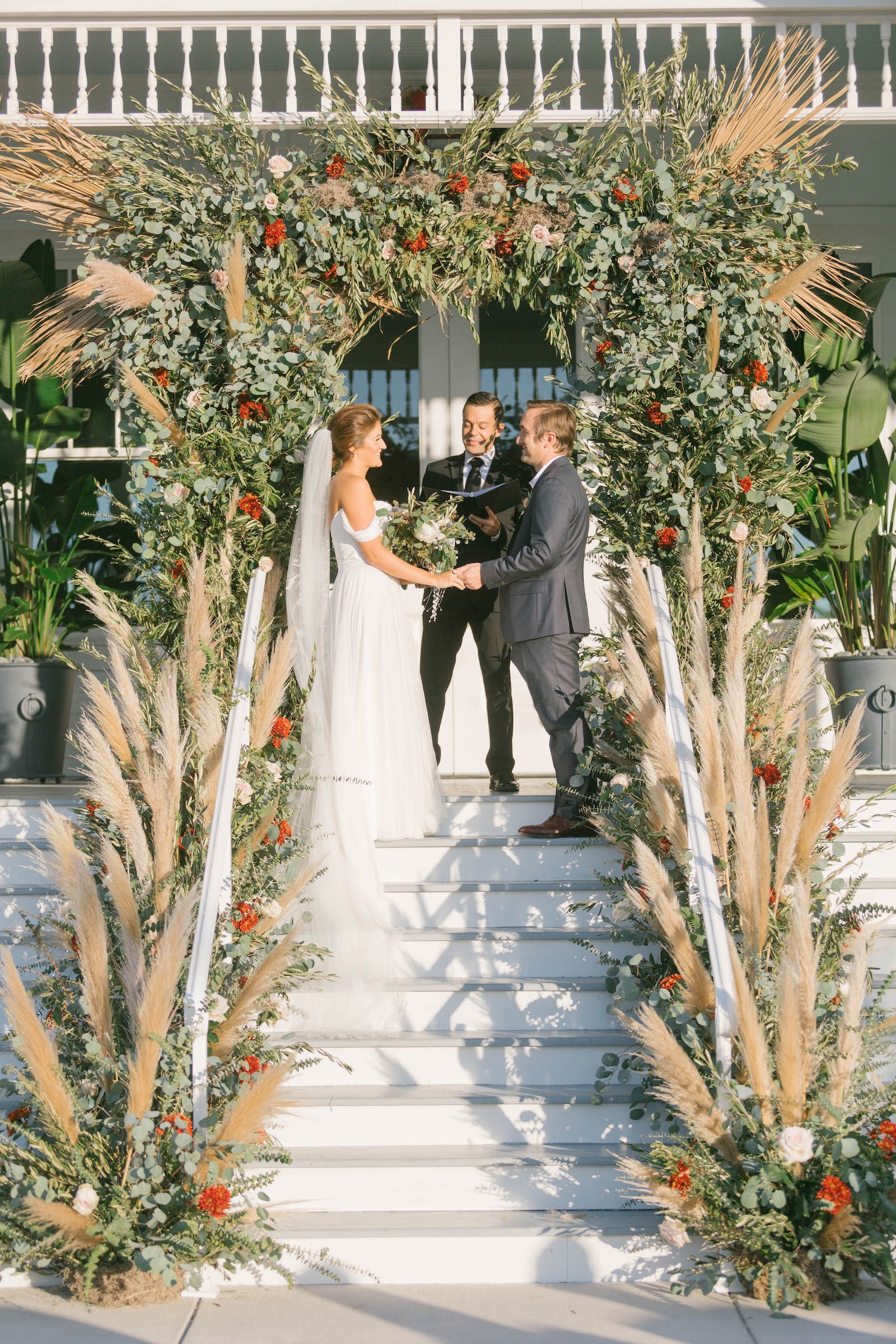 Boho Garden Wedding Ceremony, Bride and Groom Exchanging Wedding Vows Outside Florida Mansion Belleview Inn, Lush Greenery and Floral Arch with Pampas Grass Arrangements| Tampa Bay Wedding Planner Parties A'la Carte