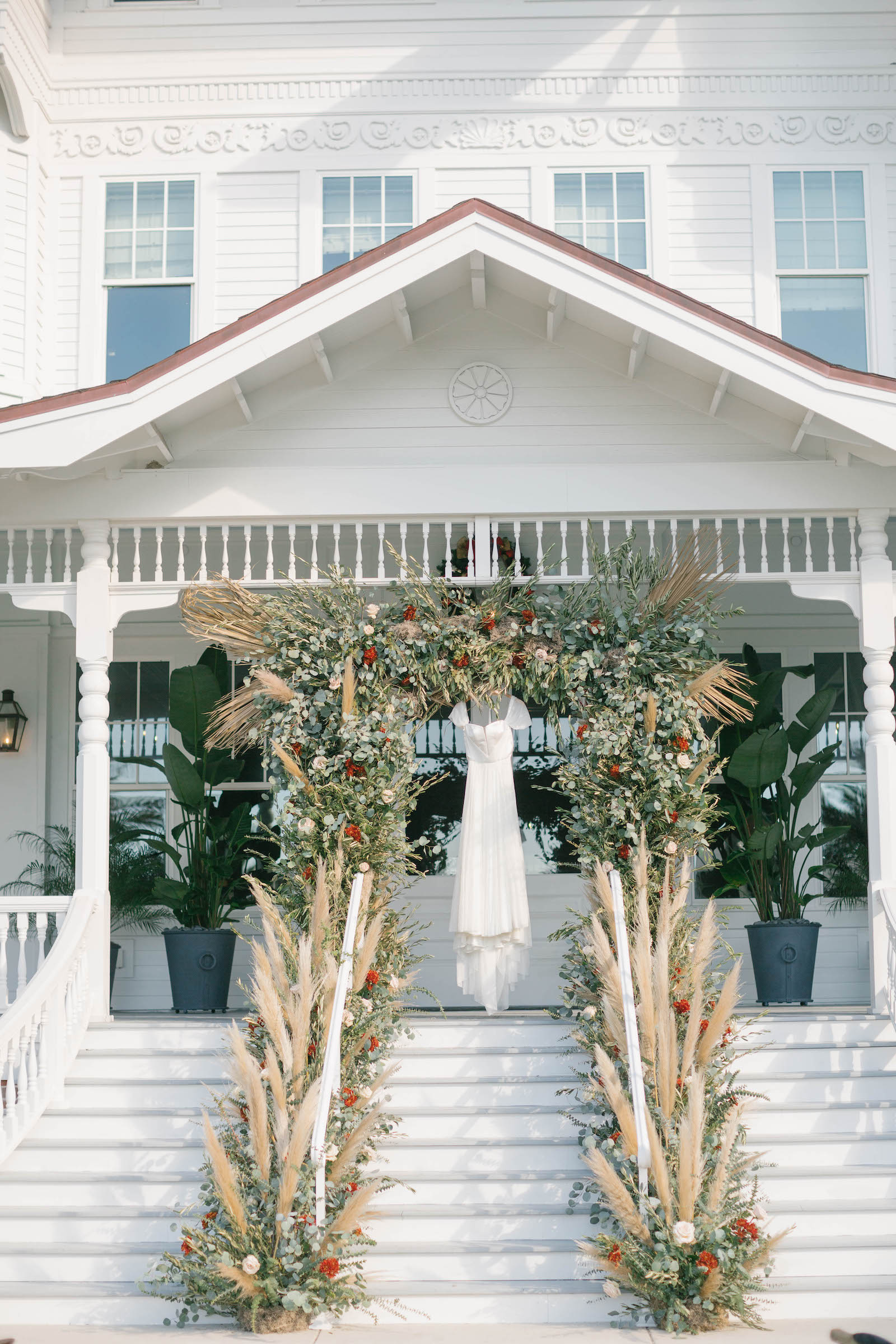 Boho Garden Wedding Ceremony, Wedding Dress Hanging On Lush Greenery and Floral Arch with Pampas Grass Arrangements, String Lights | Tampa Bay Wedding Planner Parties A'la Carte | Florida Wedding Venue Belleview Inn