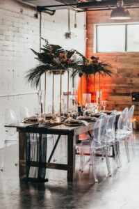 Modern Tablescape and Table Numbers with Tall Gold Centerpieces with Greenery and Tropical Flowers and Ghost Chairs | Tampa Florida Event Rentals Gabro Event Services | MDP Events Planning