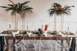 Modern Tablescape and Table Numbers with Tall Gold Centerpieces with Greenery and Tropical Flowers and Ghost Chairs | Tampa Florida Event Rentals Gabro Event Services