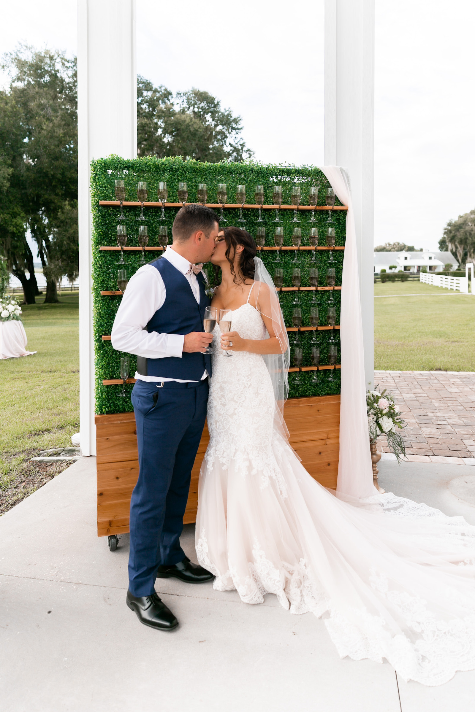 Bride and Groom Kissing In Front of Champagne Greenery Wall Wedding Portrait | Tampa Reception Covington Farms