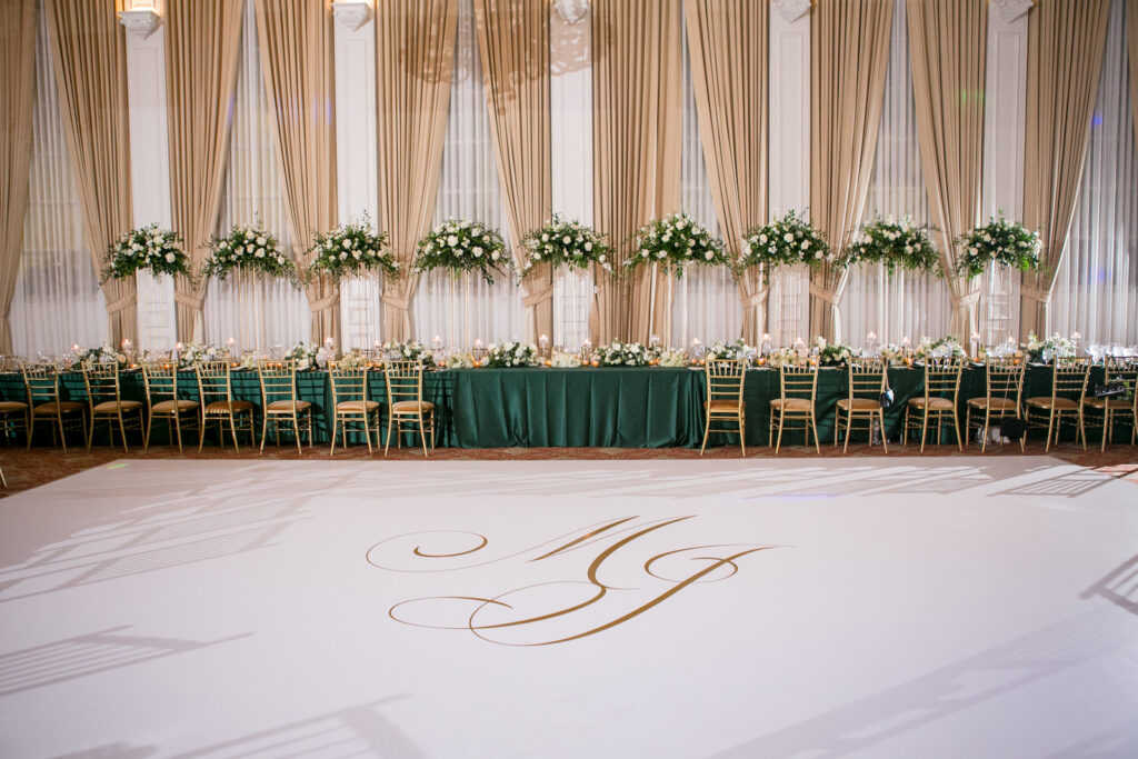 Green and Gold Christmas Wedding Decor, Long and Round Tables with Emerald Green Table Linens, Gold Chiavari Chairs, Gold Chargers, White and Greenery Low and Tall Floral Centerpieces, Gold Monogram on Dance Floor | Tampa Bay Wedding Photographer Carrie Wildes Photography | Wedding Rentals Kate Ryan Event Rentals | Over the Top Rental Linens | A Chair Affair Event Rentals