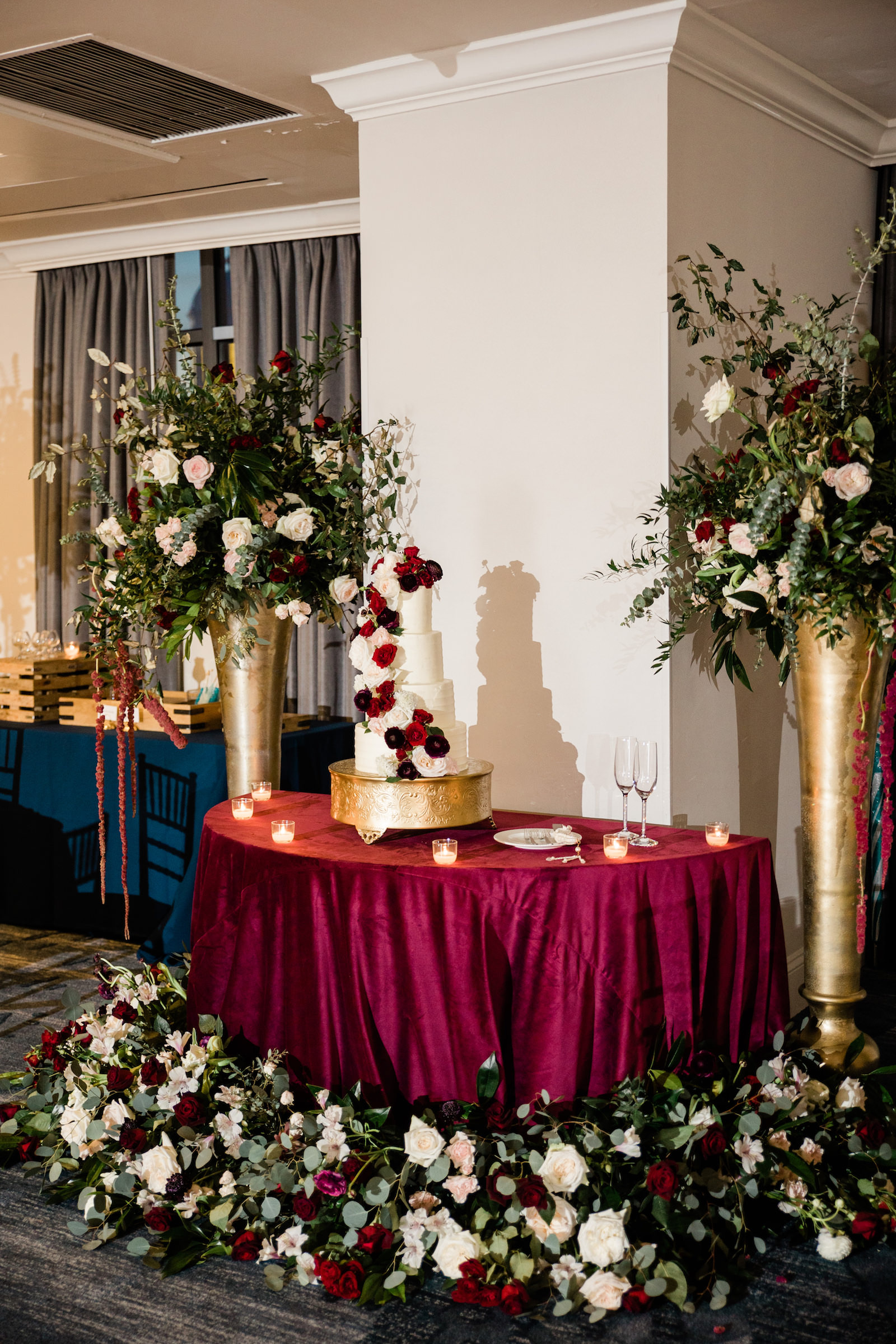 Elegant Navy Wedding Reception Decor, Cake Table with Garnet Linen, Four Tier White Wedding Cake, Tall Gold Stands with Lush Greenery, Blush Pink, Ivory, Red Flowers with Hanging Amaranthus | Tampa Bay Wedding Florist Botanica
