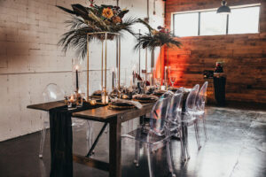 Modern Tablescape and Table Numbers with Tall Gold Centerpieces with Greenery and Tropical Flowers and Ghost Chairs | Tampa Florida Event Rentals Gabro Event Services