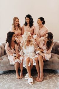 Warm Romantic Neutral Wedding, Bride Wearing White Lace Robe, Bridesmaids Wearing Blush Pin Matching Robes