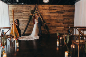 Bride and Groom First Kiss Under Wooden Triangle Arch in Industrial Wedding Ceremony | Florida Rentals Gabro Event Services