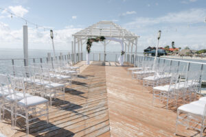 Tropical Modern Waterfront Pier Wedding Ceremony Decor, Acrylic Chiavari Chairs, White Linen Arch with Floral Arrangement | Tampa Bay Wedding Venue The Godfrey | Wedding Rentals Kate Ryan Event Rentals