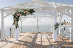 Waterfront Tropical Modern Wedding Ceremony Decor, White Linen Arch with Palm Fronds, Monstera Leaves, Pink and White Flowers | Tampa Bay Wedding Venue The Godfrey