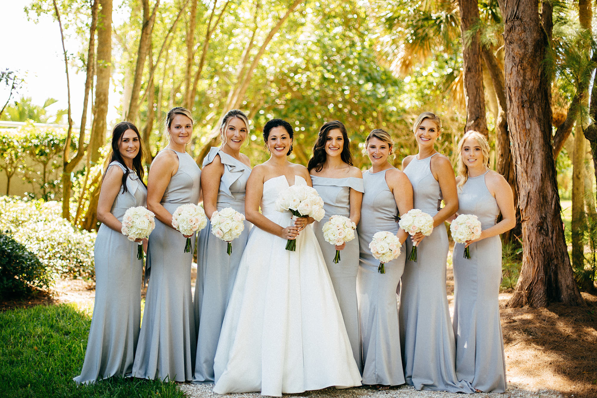 Modern Elegant Bride Wearing Strapless Classic Ballgown Wedding Dress, Bridesmaids in Silver, Gray Mix and Match Dresses Holding Round White Roses Floral Bouquets