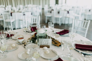 Classic White Wedding Reception with Burgundy Napkins White Flatware and Acrylic Table Numbers with Floating Candles and Greenery | Tampa Wedding Rentals Gabro Event Rentals Services