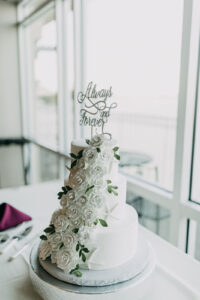 Three Tier White Wedding Cake with White Floral Details and Greenery and Cursive Cake Topper