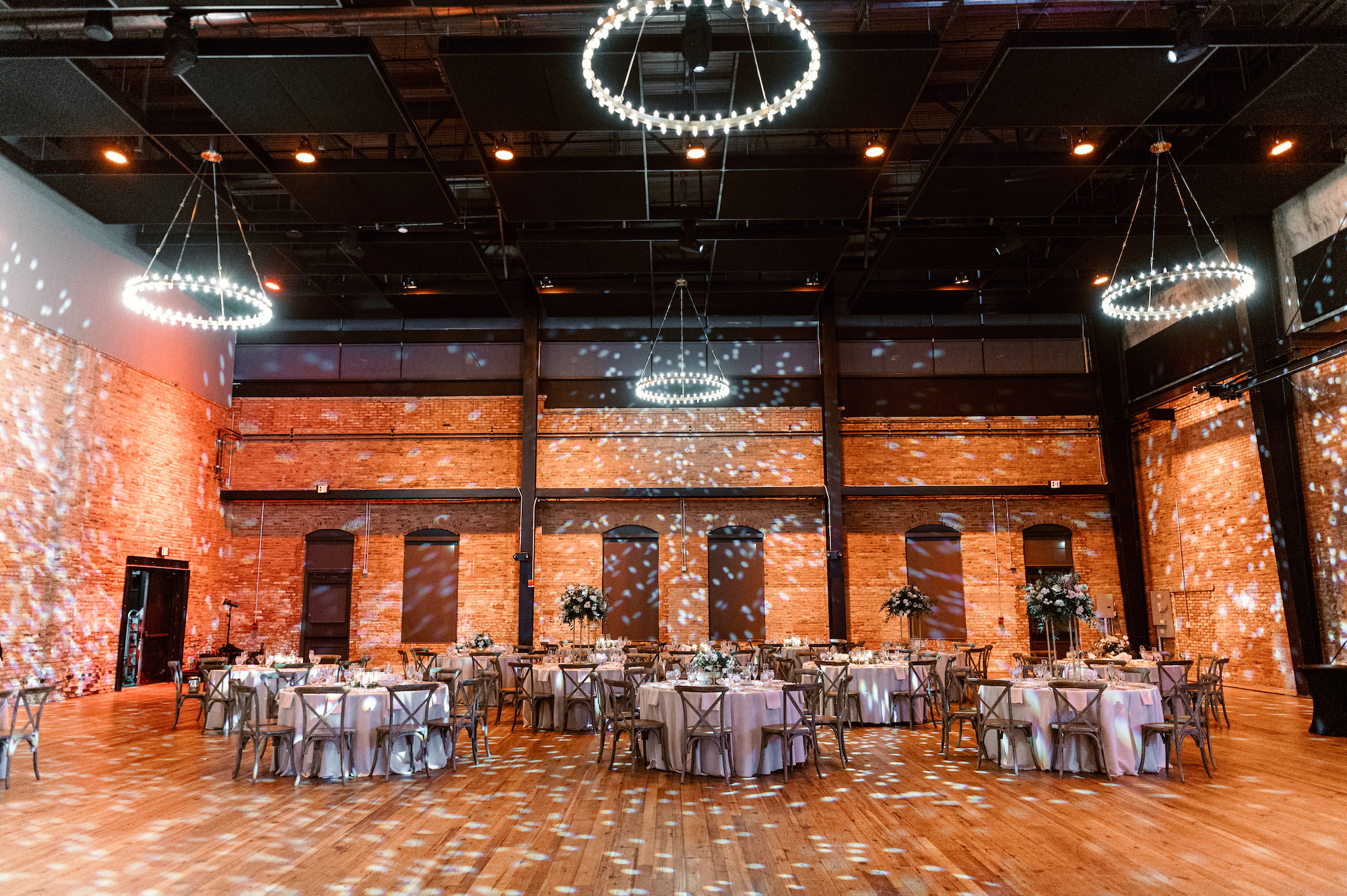 Indoor Industrial Reception with Chandeliers, Uplighting and Wooden Crossback Chairs | Tampa Wedding Armature Works The Gathering | Planner Coastal Coordinating