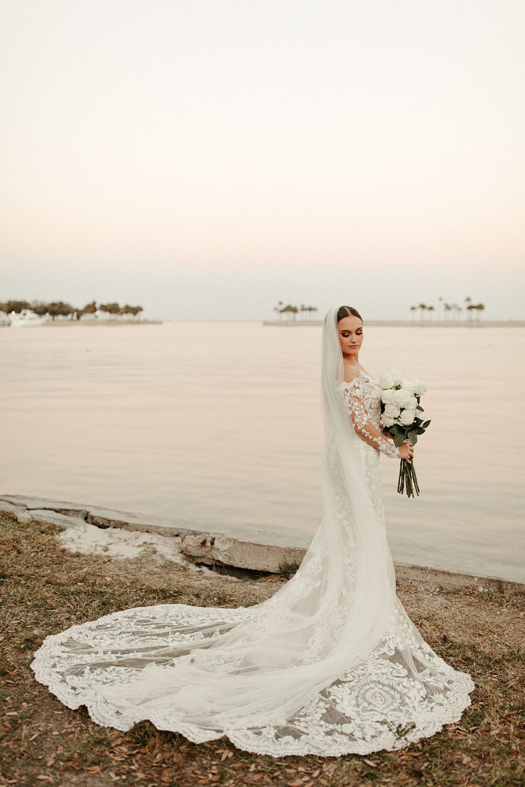 Bride in Long Sleeve Lace Sheer Wedding Dress with White Peony Bouquet and Long Train Veil Sunset Wedding Portrait