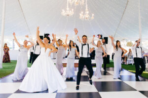 Modern Elegant Tent Wedding Reception with Hanging Chandeliers, String Lights, Live Band, Bride and Groom Dancing with Wedding Party on Black and White Checkered Dance Floor