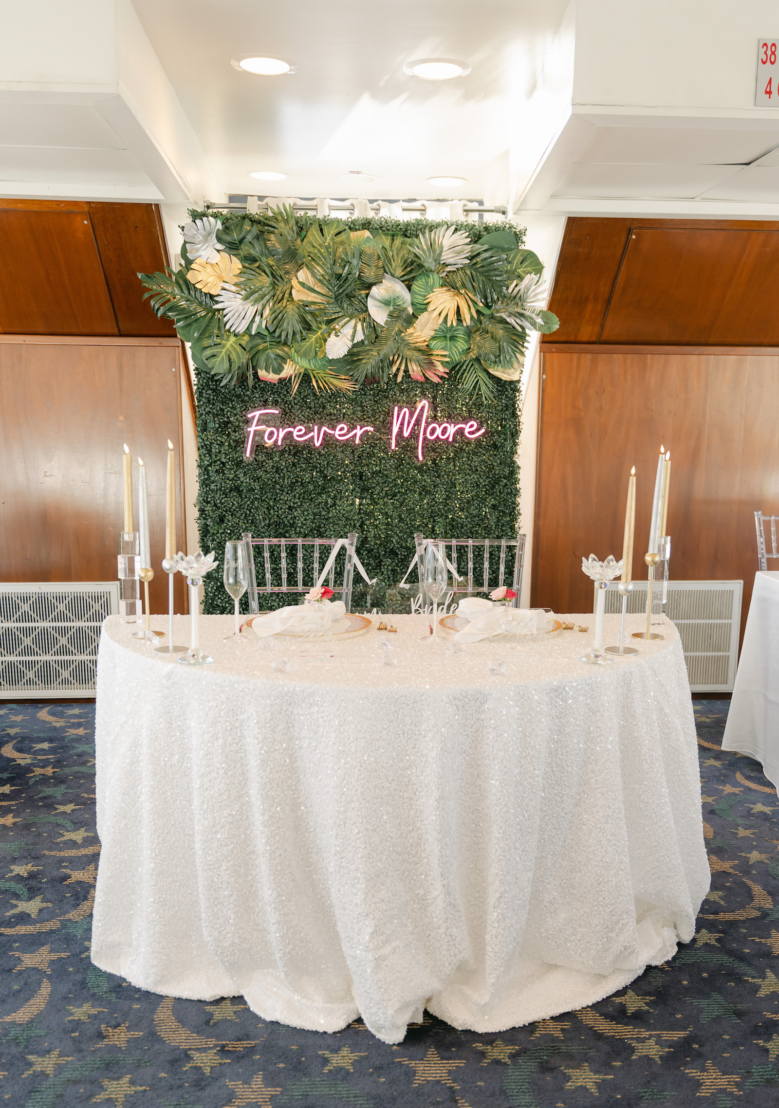 Tropical Modern Wedding Reception Decor, Greenery Hedge Wall with Pink Neon Sign with Monstera and Palm Fronds Arrangement, Sweetheart Table with White Table Linen, Candlesticks | Tampa Bay Wedding Rentals Kate Ryan Event Rentals