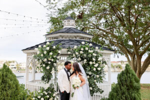 Modern Romantic Glam Bride and Groom Standing in Front of Waterfront Gazebo with Greenery and White Roses Arch | Tampa Bay Wedding Photographer Lifelong Photography Studio | Wedding Vennue Davis Islands Garden Club
