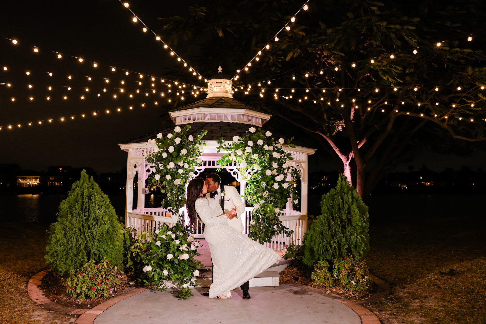 Modern Romantic Glam Wedding, Bride and Groom Kissing Under String Lights by Waterfront Gazebo with Greenery and White Roses Arch Night Portrait | Tampa Bay Wedding Photographer Lifelong Photography Studio | Wedding Venue Davis Islands Garden Club