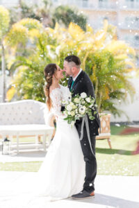 Winter Modern Whimsical Bride Wearing Long Sleeve Lace Wedding Dress and Groom KIssing with Fake Snow, White Anemone, Ivory Roses and Greenery Bridal Bouquet | Tampa Bay Wedding Dress Truly Forever Bridal