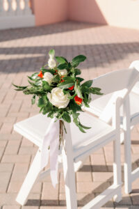 White Folding Ceremony Chair with Greenery White Floral Detail and Orange Florals | Florida Rentals Kate Ryan Event Rentals