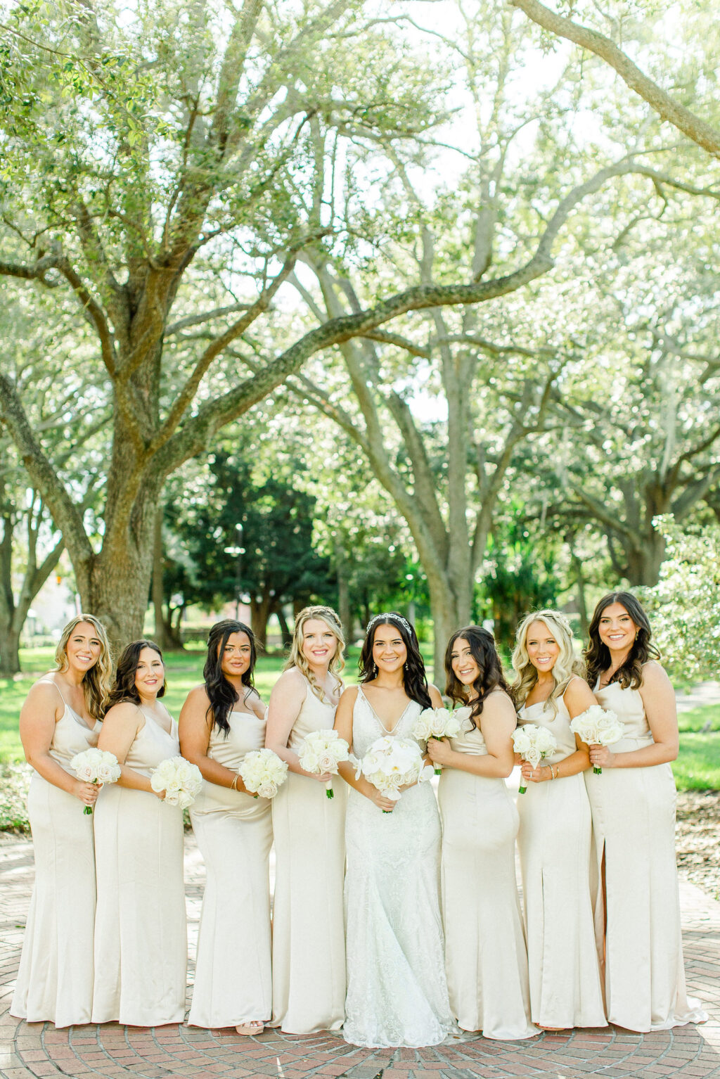 Bride Wearing Lace Fit and Flare Wedding Dress with Bridesmaids Wearing Matching Gold Dresses Holding White Floral Bouquets | Tampa Bay Wedding Hair and Makeup Femme Akoi Beauty Studio | Bridesmaids Attire Bella Bridesmaids