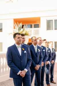 Groom and Groomsmen See Bride Walk Down the Aisle Wedding Portrait | Groom and Groomsmen in Navy Suits with Teal Bowties and Orange Boutonniere | Tampa Wedding Photographer Dewitt for Love