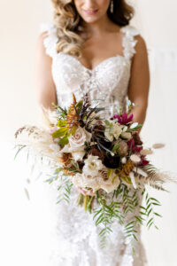 Fall Boho Bride Beauty Portrait Holding Burnt Orange, Ivory Roses, Burgundy Flowers, Greenery, Pampas Grass and Dried Leaves Floral Bouquet