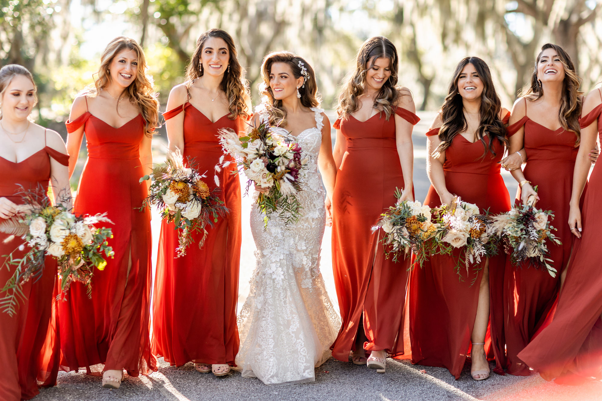 Fall Boho Bridal Party, Bride with Bridesmaids Wearing Matching Off the Shoulder Red Dresses Holding Ivory, Burnt Orange and Burgundy Floral Bouquets with Pampas Grass, Greenery and Dried Leaves