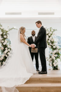 Winter Inspired Wedding, Bride and Groom Exchanging Wedding Vows During Wedding Ceremony, Greenery Pillars with White Roses Lush Floral Pillars | Tampa Bay Wedding Planner MDP Events | Safety Harbor Wedding Venue Harborside Chapel