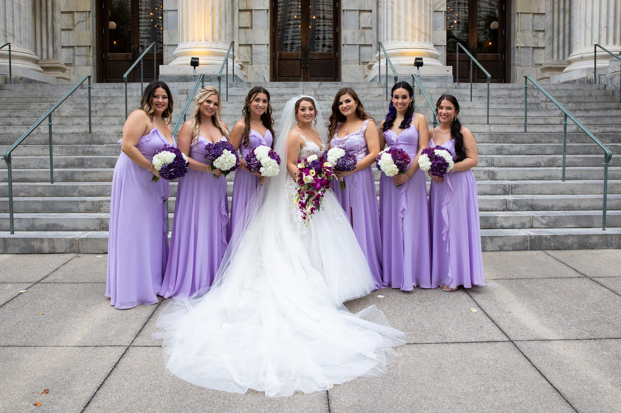 Bride and Bridesmaids in Floor Length Purple Bridesmaids Dresses Holding Purple and Cream Wedding Bouquets Portrait