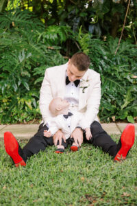 Sweet Groom and Baby Son Wearing Matching White Tuxedo Jackets, Black Bowties and Red Bottom Shoes