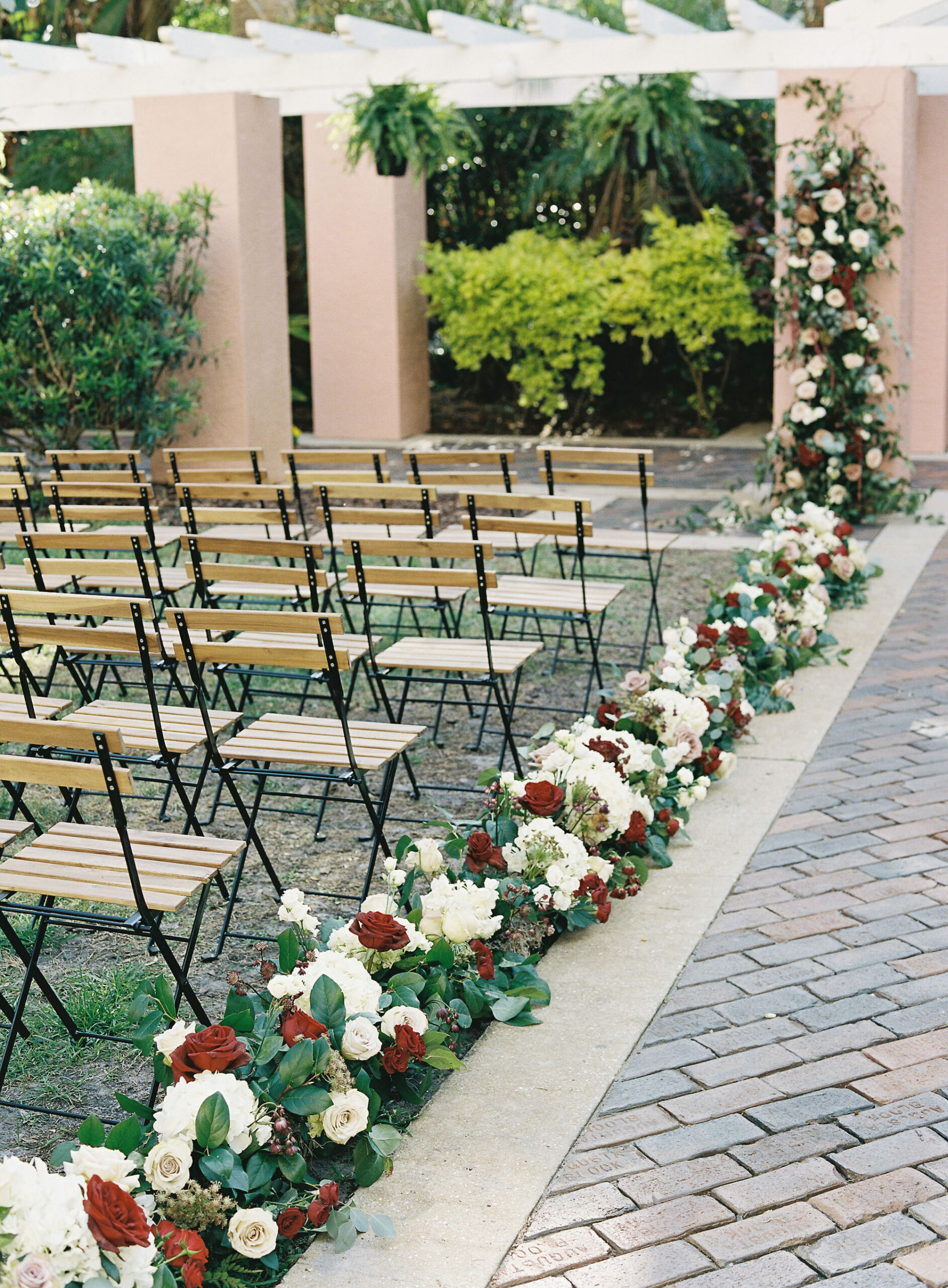Royal Glam Gatsby Elegant Wedding Ceremony Decor, Wooden Garden Chairs, Greenery and White and Red Roses Flower Arrangements Lining Aisle | Tampa Bay Wedding Planner and Designer John Campbell Weddings