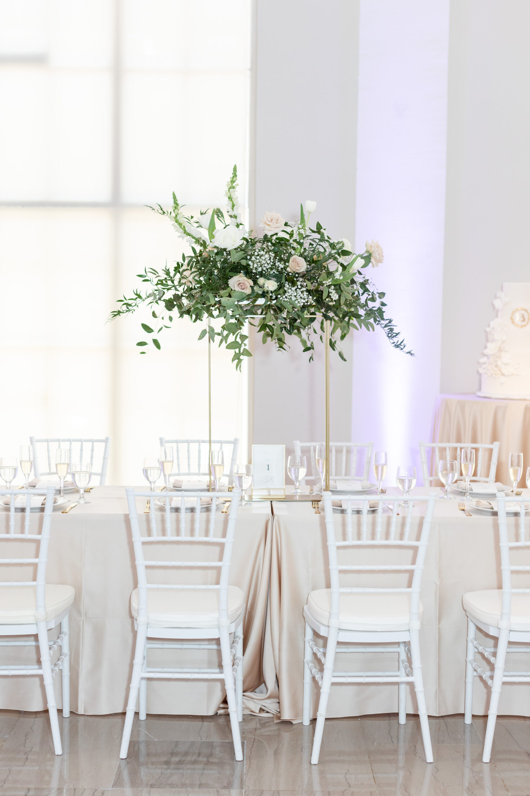 Modern Romantic Wedding Reception Decor, Champagne Table Linen, White Chiavari Chairs, Tall Gold Stands with Greenery with White and Blush Pink Floral Centerpiece