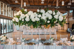 Winter Inspired Wedding Reception Decor, Long Feasting Table with Silver Table Linen, Silver Chiavari Chairs, Tall Acrylic Stands with Lush Greenery and White Hydrangeas, Roses Long Floral Centerpiece | Tampa Bay Wedding Planner MDP Events