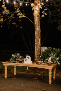 Wooden Table with Greenery and White Florals and Three Tier White Cake with Floral Detailing