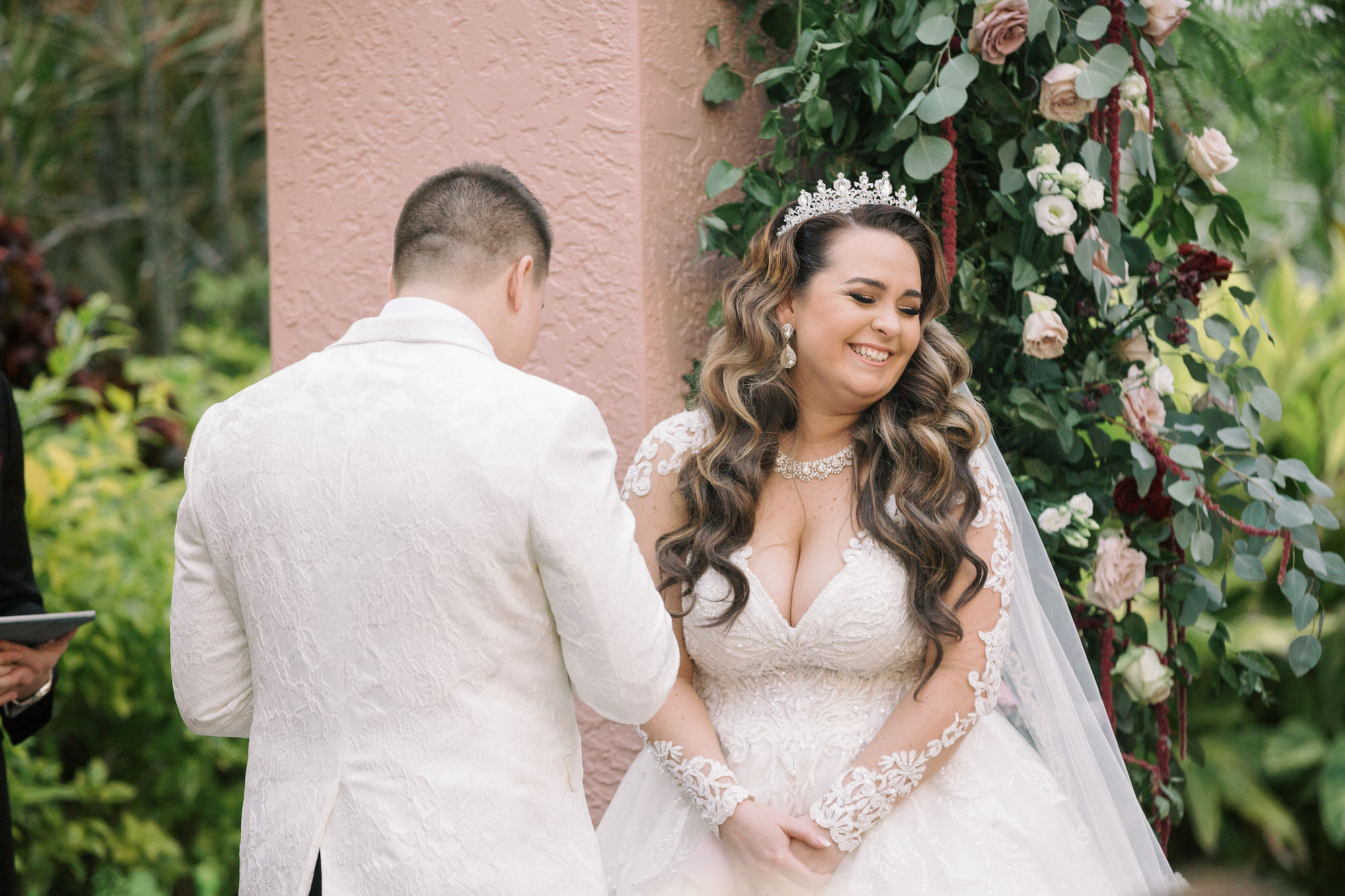 Emotionally Happy Bride Wearing Romantic Lace and Illusion Long Sleeve Deep V Neckline Wedding Dress and Princess Tiara with Veil Exchanging Wedding Vows During Ceremony | Tampa Bay Wedding Hair and Makeup Femme Akoi Beauty Studio