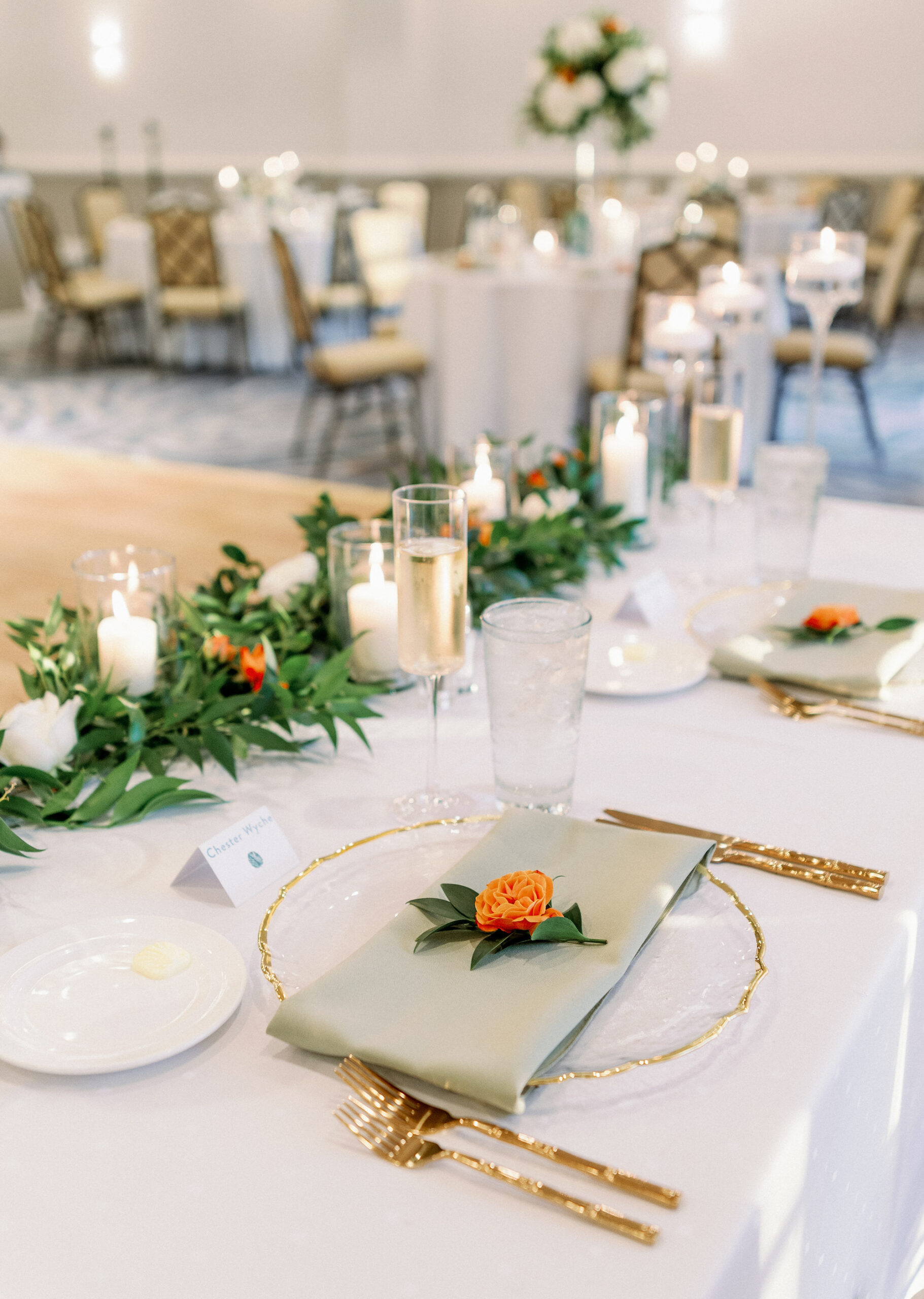 White Linen Tablescape with Greenery, Orange Floral Details and White Candles in Glass Jars and Gold Flatware | Tampa Wedding Rentals Kate Ryan Event Rentals