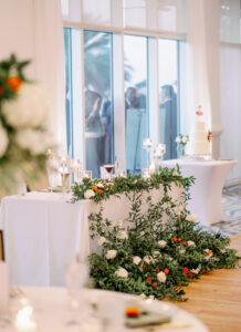 White Linen Sweetheart Tablescape with Greenery, Orange Floral Details and White Candles in Glass Jars | Tampa Wedding Rentals Kate Ryan Event Rentals
