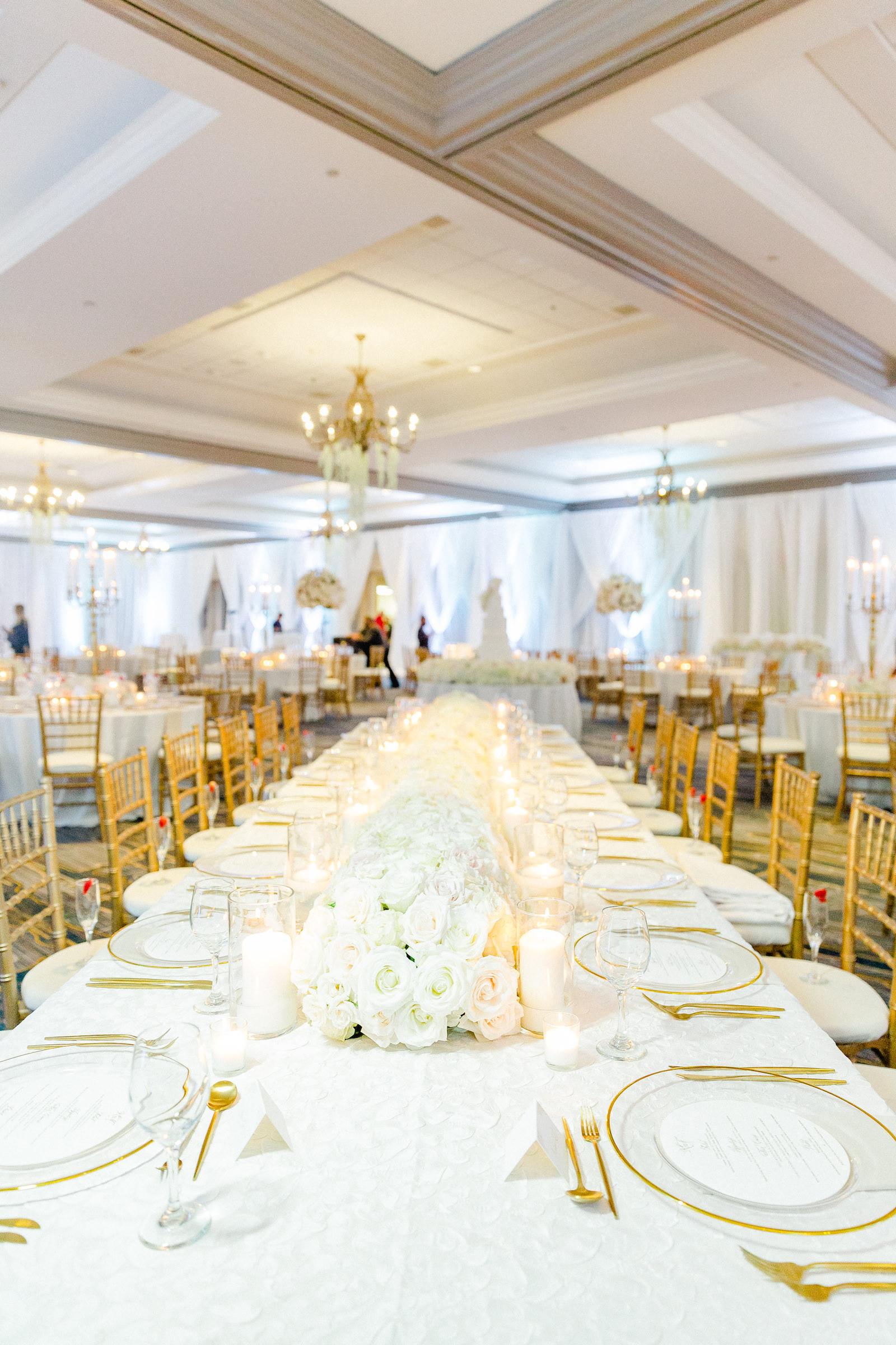 Gold and White Romantic Wedding Reception Decor, Long Feasting Table with White Table Linen, Gold Rimmed and Clear Glass Chargers, Gold Flatware, Gold Chiavari Chairs, White Roses and Hydrangeas Floral Centerpiece and Candles | Tampa Bay Wedding Florist Botanica International Design Studio