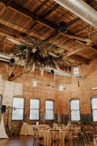 Earthy Neutral Boho Modern Chic Wedding Reception Decor, Lush Greenery, Pampas Grass Floral Hanging Chandelier, Wooden Cross Back Chairs | Tampa Bay Wedding Planner Wilder Mind Events | St. Pete Wedding Florist Save the Date Florida | Tampa Wedding Venue Armature Works