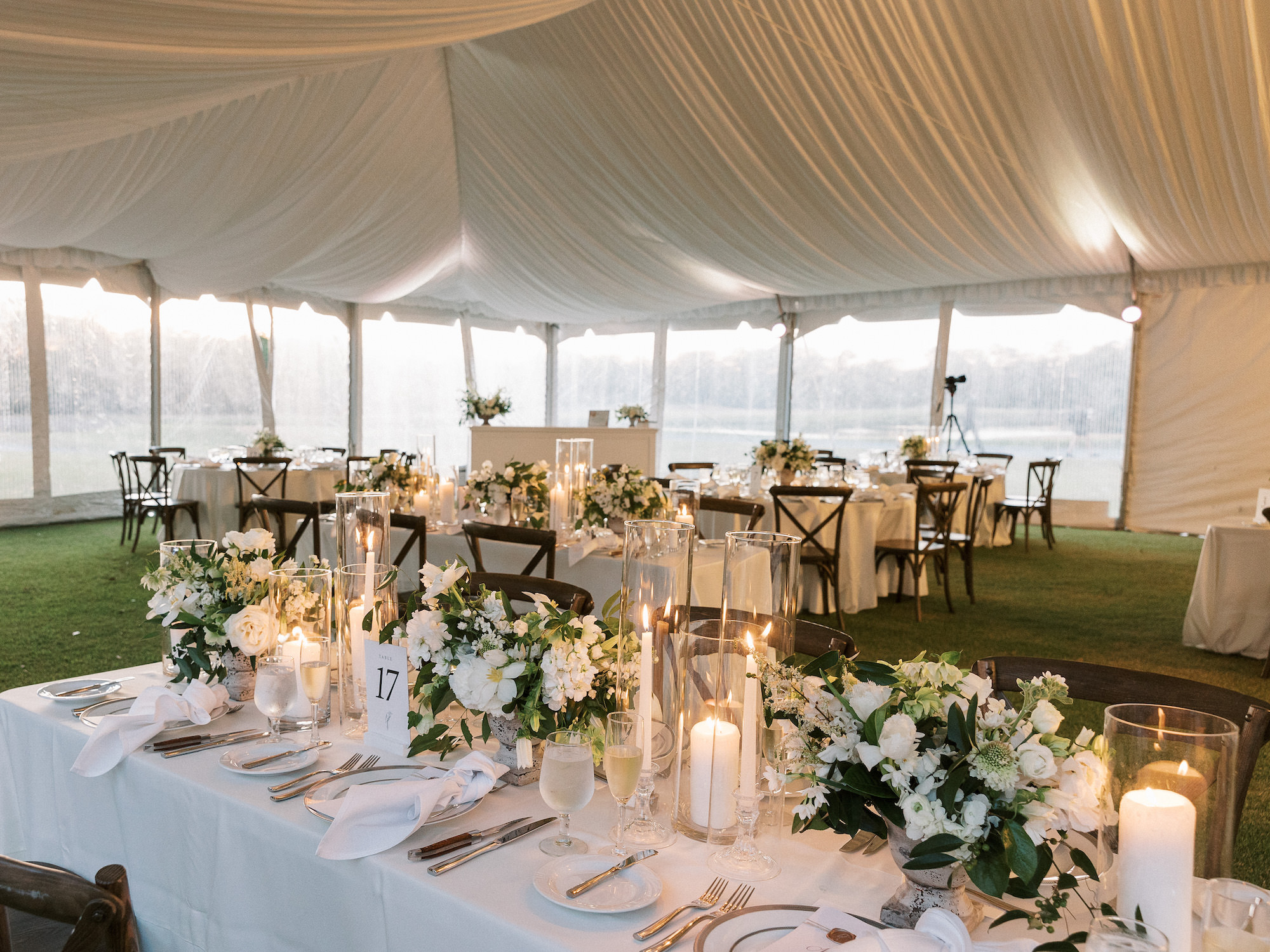 Old Florida Elegant White Tent Wedding Reception Decor, Long Tables with Wooden Cross Back Chairs, Candles, Low White Roses and Greenery Floral Centerpieces