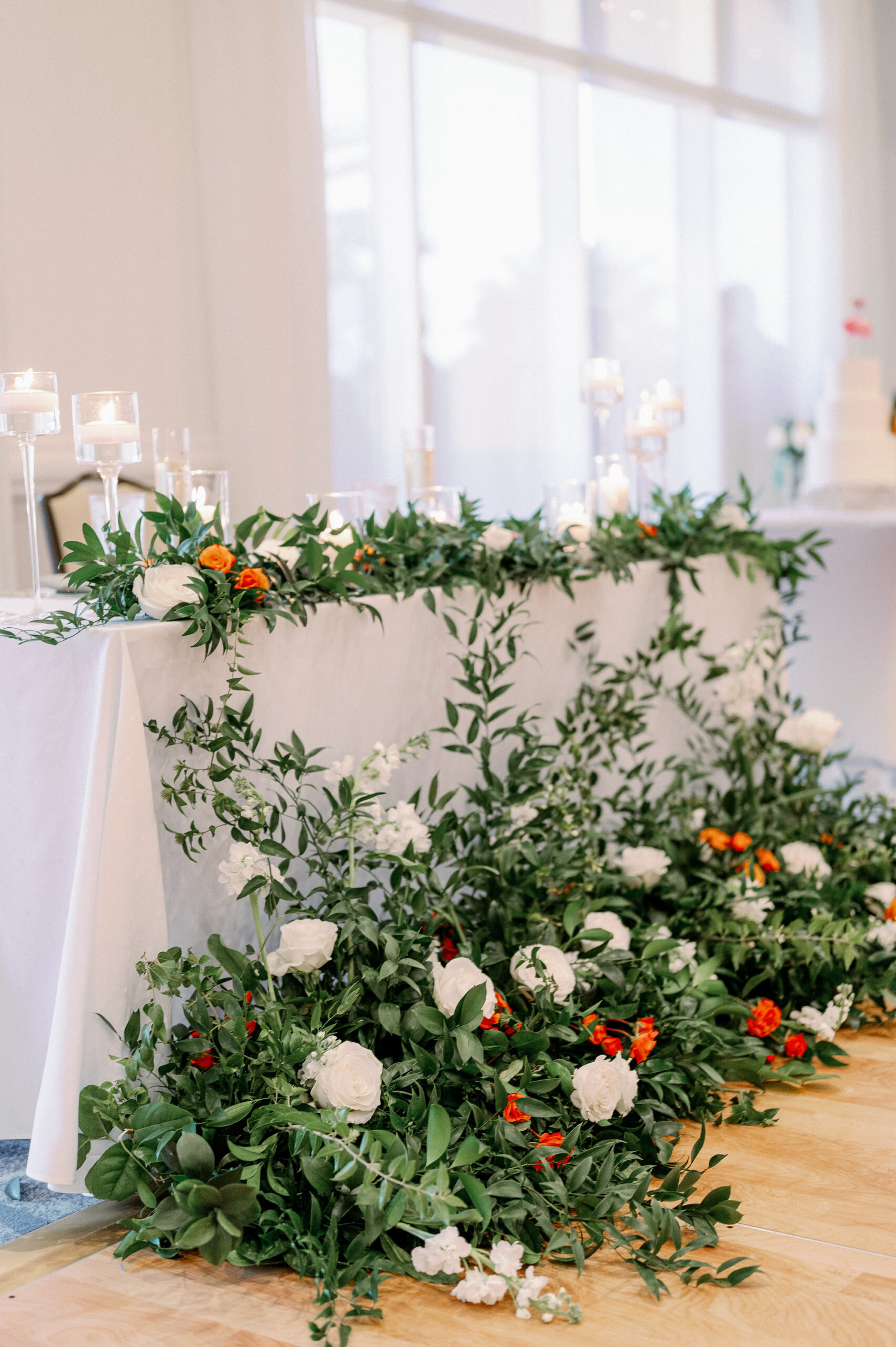 White Linen Sweetheart Tablescape with Greenery, Orange Floral Details and White Candles in Glass Jars | Tampa Wedding Rentals Kate Ryan Event Rentals