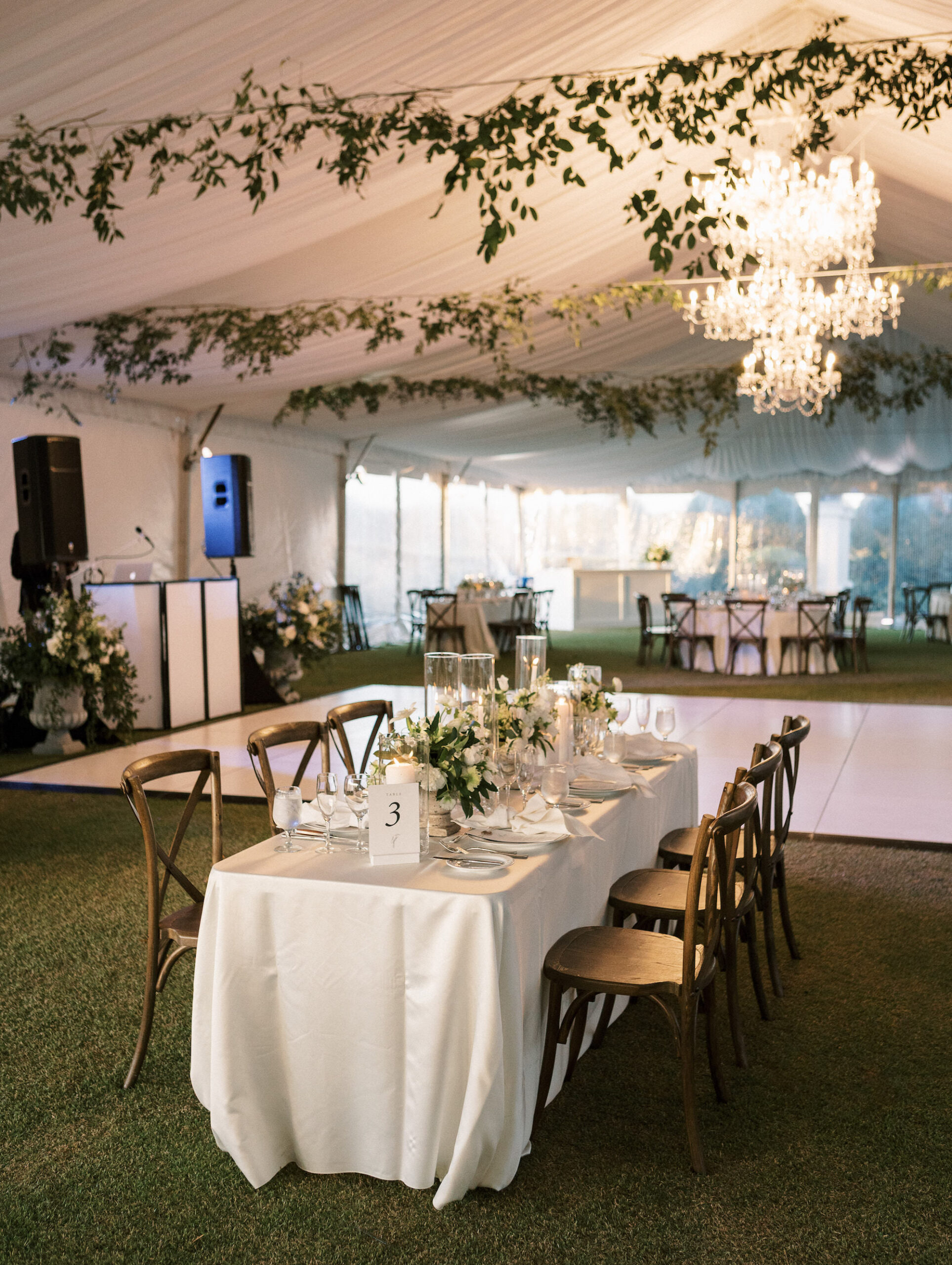 Old Florida Elegant White Tent Wedding Reception Decor, Hanging Greenery Garlands, Crystal Chandeliers, Long Tables with Wooden Cross Back Chairs, Candles, Low White Roses and Greenery Floral Centerpieces