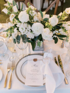 Old Florida Elegant Wedding Reception Decor, Gold Rimmed Charger Plates, Gold Silverware, White Linen Napkins, Low White Roses and Greenery Floral Centerpiece