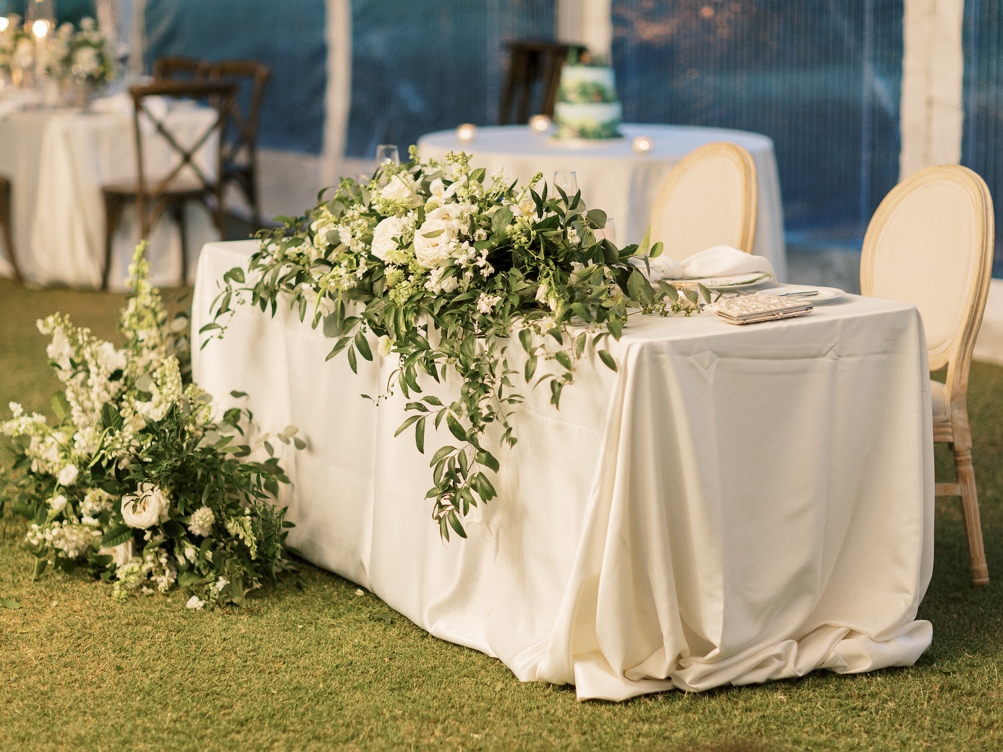Old Florida Elegant Outdoor Tent Wedding Reception Decor, Sweetheart Table with White Linen, Cream Dining Chairs, Lush Greenery and White Roses Florals