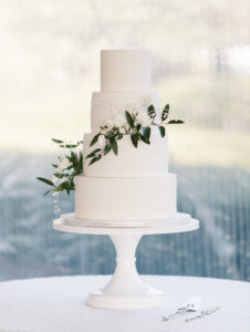 Four Tier White Wedding Cake with Cascading Greenery Leaves and White Flowers