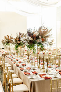 Fall Boho Wedding Reception Decor, Long Feasting Table with Champagne Table Linen, Gold Chiavari Chairs, Burnt Orange Linen Napkins, Tall Floral Centerpieces, Dried Palm Leaves, Pampas Grass, Burnt Orange, Ivory and Burgundy Florals | Tampa Bay Wedding Rentals Gabro Event Services